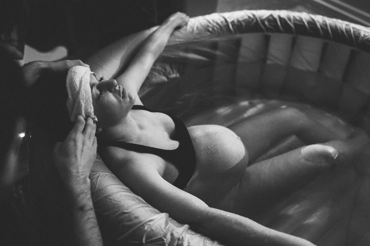 A midwife holding a cool cloth to a laboring parent's forehead in the birth pool